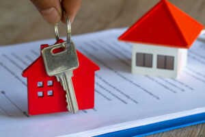 Picture of miniature houses and a key on top of a real estate contract.