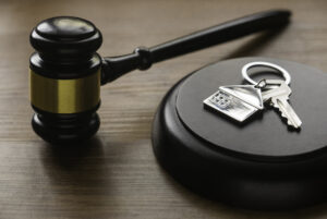 Picture of a key and a house-shaped keychain next to a gavel.