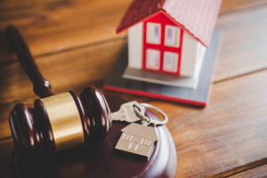 Picture of a key and a house-shaped keychain next to a gavel and a miniature house figurine.