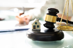 Picture of a miniature house figurine next to a gavel and the scales of justice.