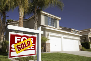 Picture of a for sale sign with a sold sticker on the front lawn of a house.