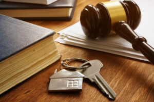 Picture of books, a silver key with a house-shaped keychain, a gavel, and a stack of papers.