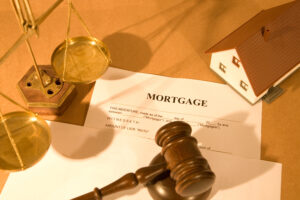 Picture of a miniature house figurine, a mortgage, a gavel, and the scales of justice.