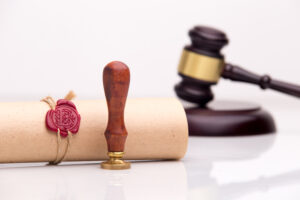 Picture of a wax seal stamp, a roll of parchment paper, and a gavel.