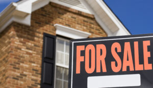 Picture of a For Sale sign in front of a brick house.