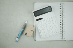 Picture of a pen, a wooden house figurine, a calculator, and a notebook.