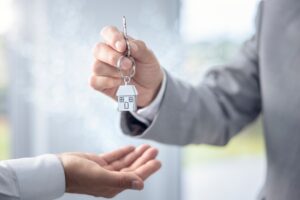 Picture of a man handing a key with a house-shaped keychain to another person.