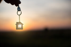 Picture of a person holding a key with a house-shaped keychain in front of a sunset.