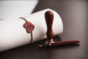 Picture of paper rolled up, tied, and sealed with wax, next to a stamp and a pen.