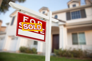 Picture of a for sale sign with a sold sticker in front of a house.