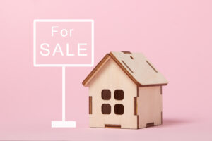 Picture of a for sale sign and a wooden house figurine.