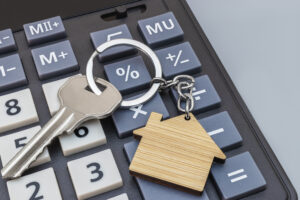 Picture of a key and a house-shaped keychain on top of a calculator.