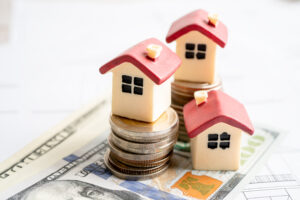 Picture of three miniature house figurines on top of stacks of coins and cash.