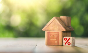 Picture of a wooden house figurine next to a wooden block with a red percentage sign on its side.