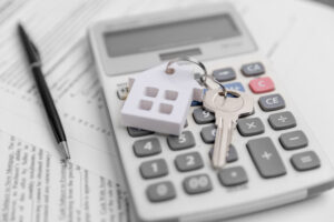 Picture of a key with a house-shaped keychain, a calculator, a pen, and mortgage papers.