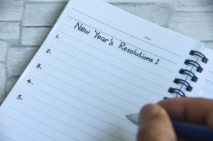 Picture of a person writing in a notebook with "New Year's Resolutions" written at the top of the page.