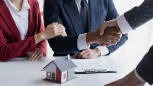 Picture of a foreclosure defense lawyer shaking a client's hand with a house figurine and a clipboard on the desk below them.