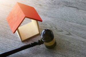 Picture of a wooden house figurine and a gavel on a wood table.