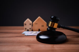 Picture of a gavel, money, and two wooden house figurines sitting on a wooden table.