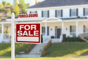 Picture of a foreclosure sale sign posted in front of a large white house.