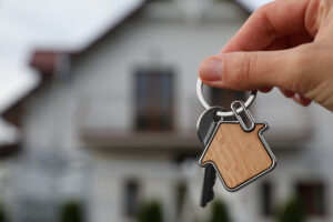 Picture of a person holding a key and a house-shaped keychain in front of a house.