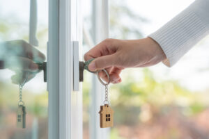 Picture of a woman using a key with a house-shaped keychain to open a door.