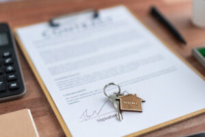 Picture of a key and a house-shaped keychain sitting on top of a clipboard with closing paperwork.