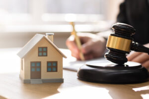 Picture of a house figurine and a gavel with a real estate attorney writing on a piece of paper in the background.