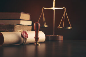 Picture of law books, a rolled piece of parchment with a wax stamp, and the scales of justice.