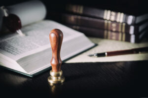 Picture of a wax stamp, a pen, paper, and law books.