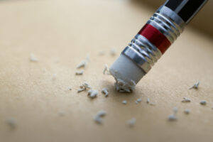 Picture of a pencil erasing writing on a sheet of paper.